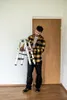 A man is holding a folded step ladder in a room with a wooden door and white walls. Produktbild-Vorschau