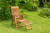 A wooden deck chair with an extended footrest sits on a lush green lawn in a garden setting. Podgląd zdjęcia produktu
