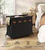 A black laundry basket with multiple compartments is shown in a bedroom setting, next to a nightstand and bed. The basket is filled with laundry and has labels on the front. Produktbild-Vorschau