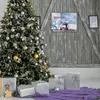 A decorated Christmas tree with gifts underneath, set against a rustic wooden wall. Produktbild-Vorschau