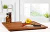 A wooden cutting board with various ingredients and a knife on it, placed in a kitchen setting with a window in the background. Produktbild-Vorschau