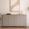 A modern gray sideboard with fluted doors is displayed in a room with artwork on the wall and a lamp in the background.