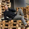 A man is sitting on a stack of wooden pallets, talking on his phone. Náhled obrázku produktu