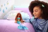A young girl with curly hair is looking at a mermaid doll on a bed. Podgląd zdjęcia produktu
