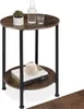 A two-tiered round side table with a wood-grain finish and black metal legs, decorated with a plant, a bottle of water, a glass, and books. Náhled obrázku produktu