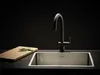 A modern kitchen sink with a black faucet and a wooden cutting board with rosemary on a dark countertop. Produktbild-Vorschau