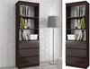 Two identical dark brown bookshelves are shown side-by-side against a textured white wall. A floor lamp with a grey shade stands between them. The bookshelves are filled with books and one has a white storage box. Podgląd zdjęcia produktu