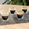 Four double-walled espresso cups filled with dark espresso sit on a textured mat on a wooden table. Anteprima dell’immagine prodotto