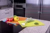 A kitchen counter with several colorful cutting mats, tomatoes, bell peppers, and green onions. Produktbild-Vorschau