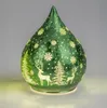 A green glass teardrop-shaped decorative lamp with a frosted winter scene featuring reindeer and trees, illuminated from within. Produktbild-Vorschau