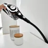 A hand holding a cordless vacuum cleaner, demonstrating its use on a white surface next to two decorative jars. Produktbild-Vorschau