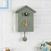 A green cuckoo clock with a pendulum hangs on a white brick wall. Náhľad obrázku produktu