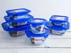 A collection of Pyrex glass food storage containers with blue lids, stacked on a white wooden surface. Anteprima dell’immagine prodotto
