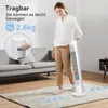 A woman is standing in a living room, holding a white tower fan. The fan is on a rug on the floor. Produktbild-Vorschau