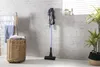 A vacuum cleaner is standing in a bathroom next to a laundry basket and a plant. Voir les images du produit