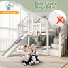 Two young children are sitting on the floor in front of a white bunk bed with a slide and stairs. The bunk bed has a house-like design with windows and a forest-themed wallpaper on the back wall. The children are holding stuffed animals. Náhled obrázku produktu