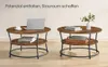 Two round coffee tables with a rustic wood finish and black metal legs are shown in a room setting. The tables have a lower shelf for storage. The left table has a laptop and a cup of coffee on it, while the right table has books and a decorative basket wi Produktbild-Vorschau