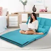 A woman is using a laptop while sitting on a blue floor sofa in a bedroom. Produktbild-Vorschau