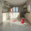 A woman is mopping a marble floor in a bright, modern kitchen with large windows overlooking the ocean. Produktbild-Vorschau