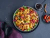 A salad with grilled cheese, plums, and nuts, served with a dark sauce and cinnamon sticks. Produktbild-Vorschau