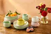 A collection of ceramic tableware and fruit arranged on a wooden table, with flowers in a vase in the background. Anteprima dell’immagine prodotto