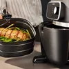 A person is holding a basket of food from an air fryer, with the air fryer itself visible. Podgląd zdjęcia produktu