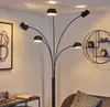A modern floor lamp with multiple adjustable arms and shades is shown in a room setting, next to a framed abstract artwork and a small side table with a book and drink. Produktbild-Vorschau