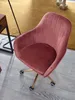 A pink velvet office chair with gold legs and wheels is shown on a wooden floor with a yellow rug in the background. Produktbild-Vorschau