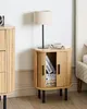 A bedside table with a lamp and books on top, next to a bed. Náhľad obrázku produktu