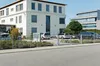 A view of a modern office building with a parking lot in front, separated by a fence. Produktbild-Vorschau