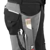 A close-up view of the side pocket of work pants, showing tools like a folding ruler and a utility knife stored in the pockets. Produktbild-Vorschau