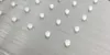A close-up view of small white cylindrical objects arranged in a grid pattern on a brushed metal surface. Podgląd zdjęcia produktu
