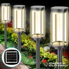 Four solar-powered garden lights are illuminated in a garden setting with flowers and greenery. Anteprima dell’immagine prodotto