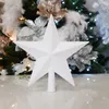 A white star-shaped tree topper is placed on a reflective surface in front of a decorated Christmas tree. Anteprima dell’immagine prodotto