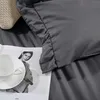 A close-up of a gray duvet cover with a ruffled edge, a white teacup and saucer on a magazine, and a textured beige throw blanket. Podgląd zdjęcia produktu