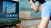 A man wearing headphones is looking at a computer screen, which displays video editing software. Produktbild-Vorschau
