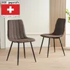 Two brown upholstered dining chairs with black metal legs are shown in a room with a light-colored wall and wooden paneling. Produktbild-Vorschau
