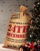 A large burlap sack with Christmas-themed text and decorations, next to a decorated Christmas tree. Produktbild-Vorschau