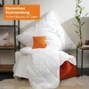 A bed with pillows and a blanket, styled with a plant and a shelf in the background. Produktbild-Vorschau