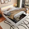 A white upholstered bed with storage is shown with the storage compartment open, revealing items inside. The bed is made up with bedding and blankets. Náhled obrázku produktu