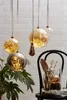 Several glass baubles filled with fairy lights are hanging in front of a brick wall, with a plant and a chair with decorative items in the foreground. Produktbild-Vorschau