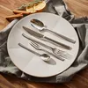 A set of cutlery is arranged on a white plate, with cinnamon sticks and dried orange slices in the background. Anteprima dell’immagine prodotto