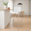 A white bar stool is shown in a bright, modern interior setting, with a kitchen counter to the left and a dining area in the background. Podgląd zdjęcia produktu