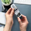 Hands holding a bottle of black ink on a desk with a keyboard and notebook. Produktbild-Vorschau