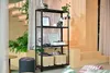 A shelving unit filled with decorative items and storage baskets, placed next to a staircase and plants in a room. Náhled obrázku produktu