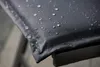 Close-up of a dark gray cushion with water droplets on it, resting on a black metal frame. Produktbild-Vorschau