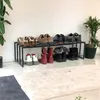 A shoe rack with various shoes and boots arranged on it, placed against a white wall next to a potted plant. Podgląd zdjęcia produktu