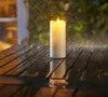 A lit LED candle sits on a wet wooden table outdoors during a rain shower. Produktbild-Vorschau