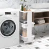 A white rolling cart with three shelves is placed next to a white washing machine in a bathroom. Produktbild-Vorschau