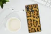 A leopard print phone case is shown on a white desk next to a cup of coffee and earphones. Produktbild-Vorschau